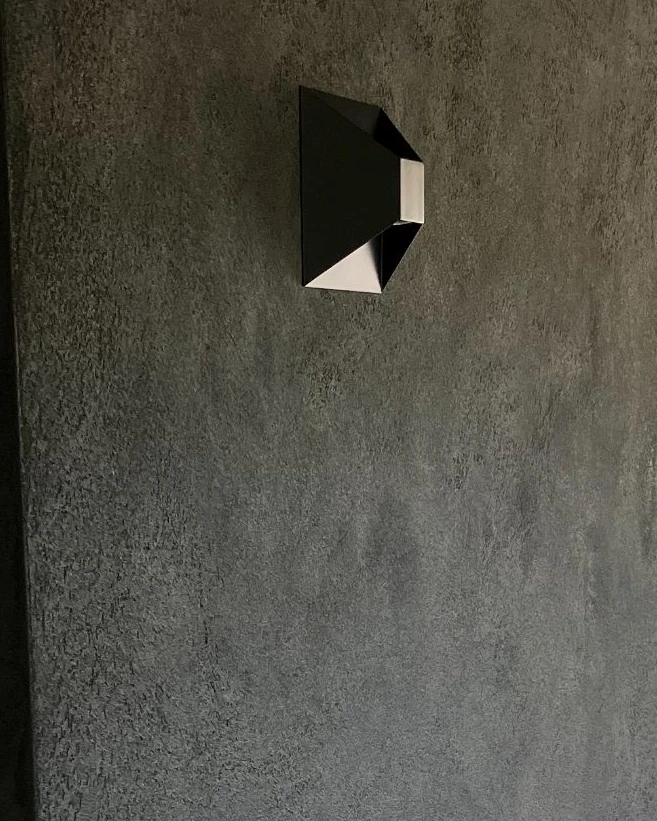 Donkergrijze wand in Tusk, een stuctechniek met grof gemalen glasparels, naast een hoekige designwandlamp