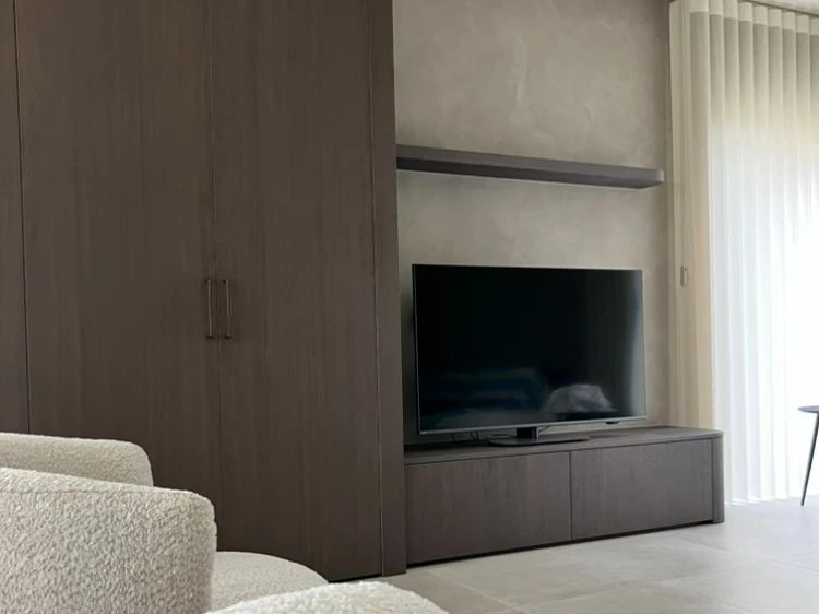 Grijze stucwand achter de televisie, naast een houten kastwand